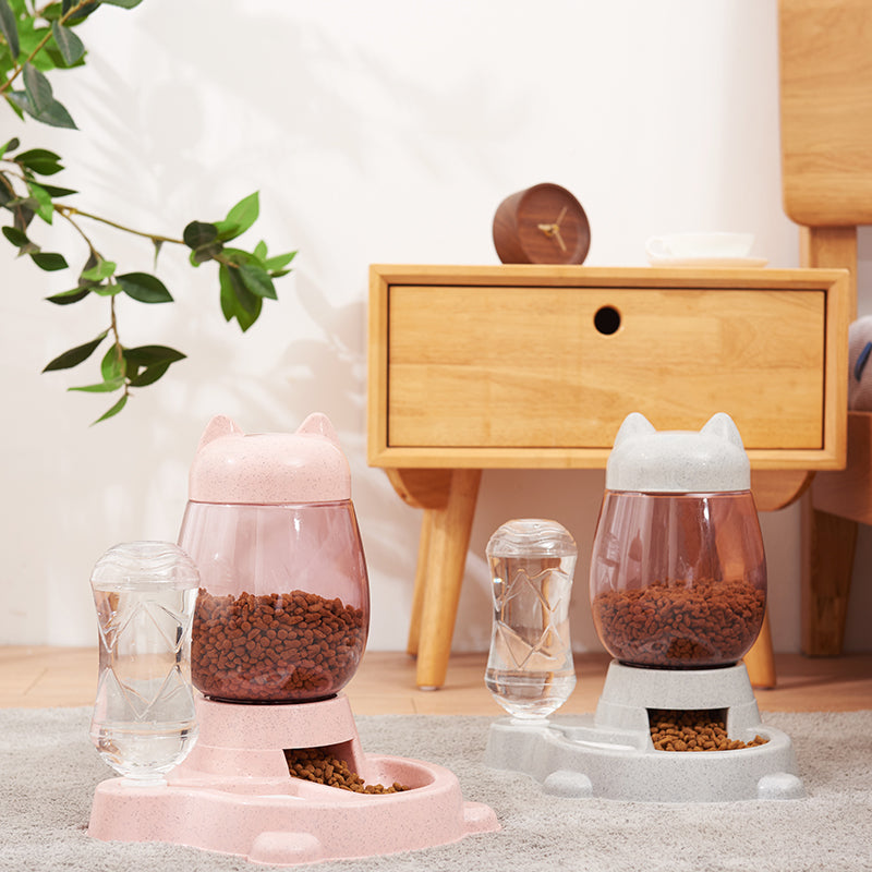 Two pet feeders, one pink and one white, on a surface with a wooden cabinet in the background.