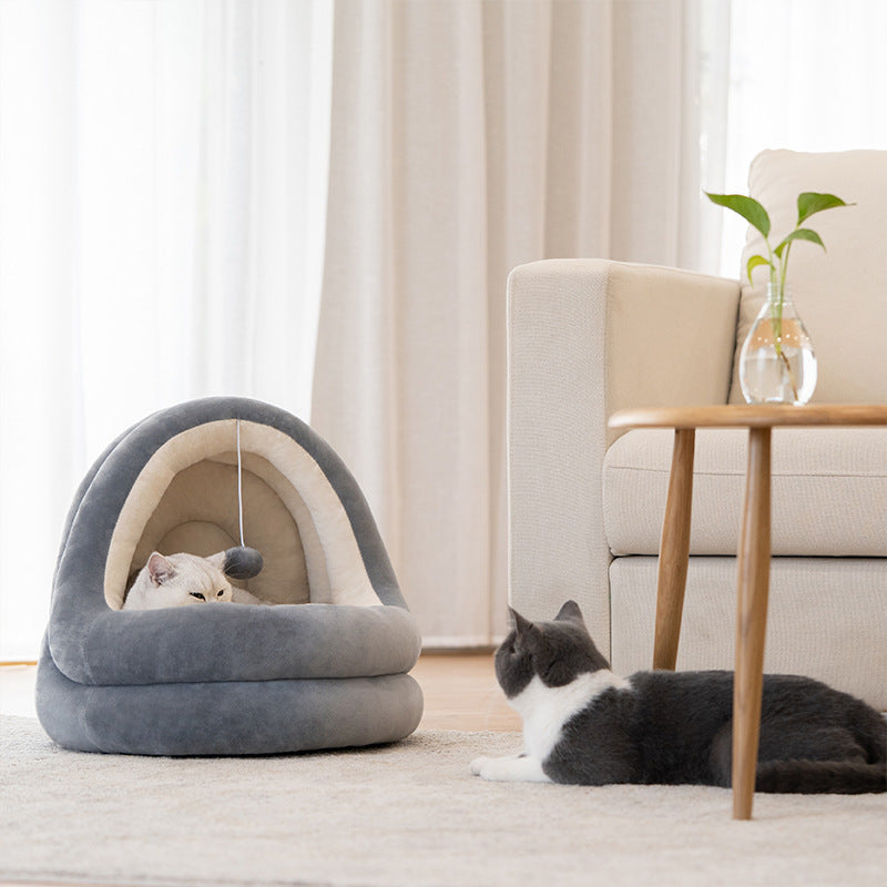 Cat lying in a gray pet bed in a cozy living room with a cat sitting on the floor.