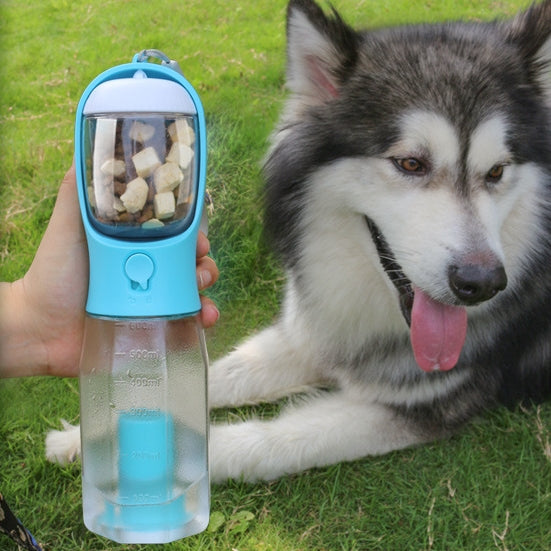 Pet water bottle with treats held by a person, with a dog lying on grass in the background
